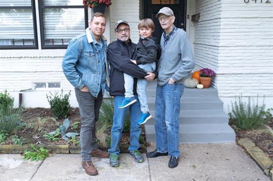 Four family members pose together outside a welcoming home surrounded by plants and decorations.