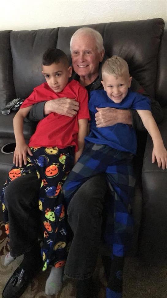 A grandfather happily embraces his two grandsons while they sit together on a couch.