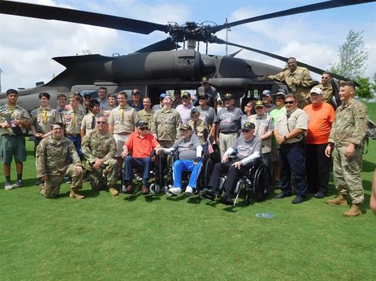 Veterans, service members, and supporters gather by a helicopter on a sunny day.