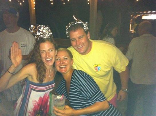 Three friends pose joyfully at a lively evening event, celebrating together with drinks.