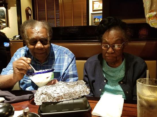 Two elderly individuals share a meal, smiling and engaged with their food at a cozy restaurant.
