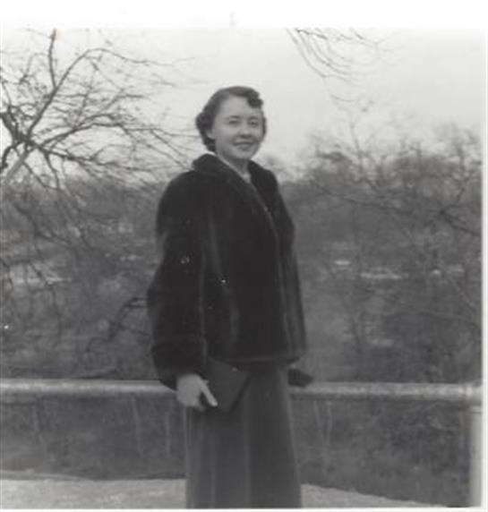 An elegantly dressed woman smiles on a balcony, enjoying the winter scenery.