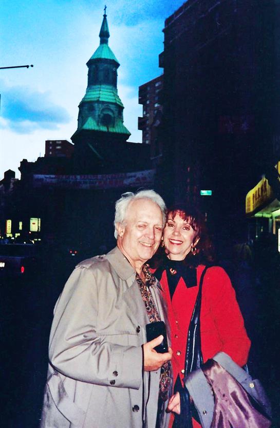 A happy couple enjoys a moment together near a lit historical building as dusk falls.