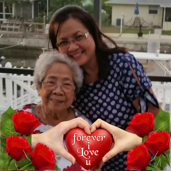 Two women happily pose by the water, surrounded by roses and a heart, sharing a moment of love.