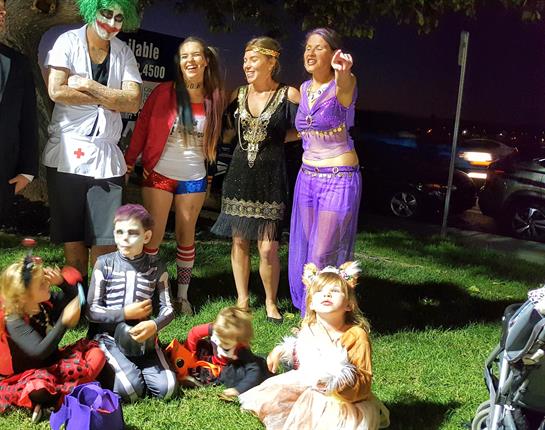 A lively group dressed in various costumes gathers for Halloween fun in a park under night lights.
