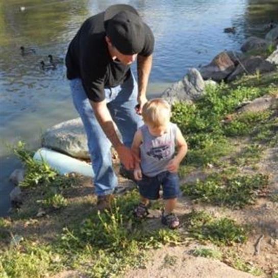 A grandfather holds the hand of his small grandson as they walk along a riverbank.