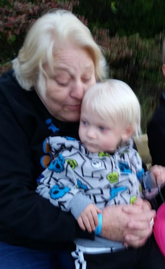 A grandmother kisses her young grandchild while sitting outdoors, creating a heartwarming moment.