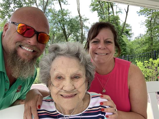 Two family members pose happily with an elderly woman, smiles bright under the sunny sky.
