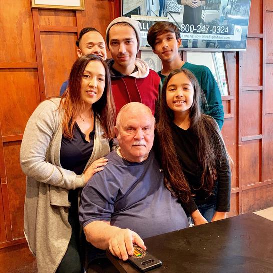 A grandfather smiles with his daughter and grandchildren at a restaurant.