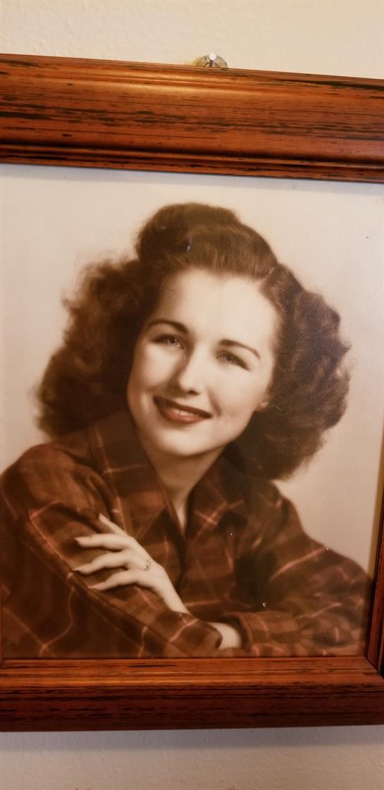 A woman with curly hair poses happily, dressed in a plaid shirt against a nostalgic backdrop.