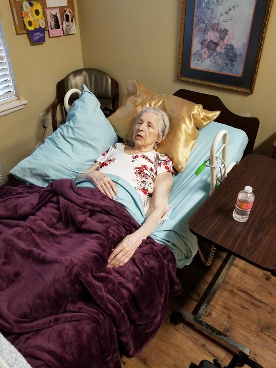 Senior woman lies in bed, surrounded by soft pillows and a warm blanket, enjoying a quiet moment.