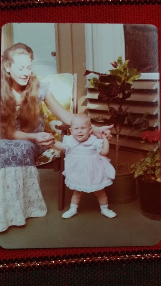 A happy mother assists her baby in taking first steps in a cozy, plant-filled room.