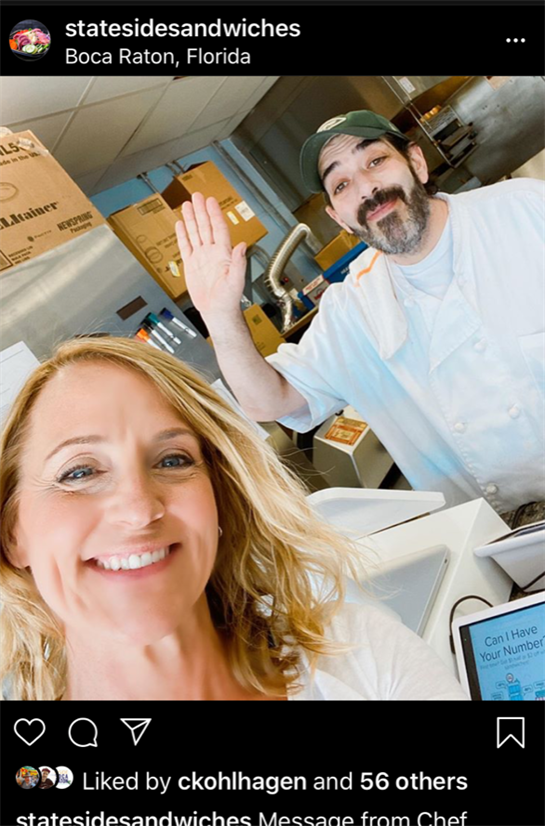Customer takes selfie with staff member at restaurant's bustling kitchen during lunch service.