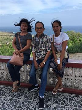 Three people enjoy the breeze together at a viewpoint with a stunning coastal backdrop.