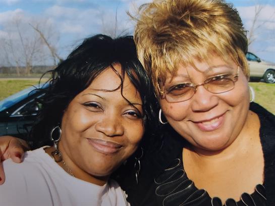 Two women pose happily together outside with bright smiles and relaxed expressions.