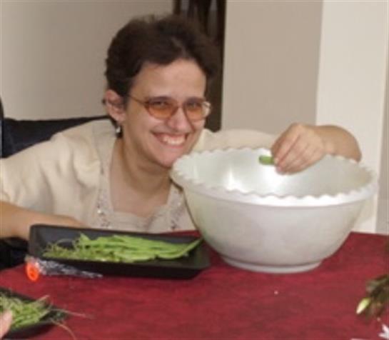 A joyful woman organizes fresh vegetables in a large bowl at a home kitchen.