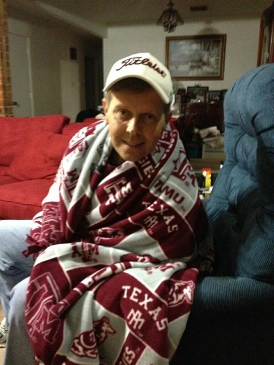 A person sits comfortably on a chair, cozy in a Texas A&M blanket during a cool evening.