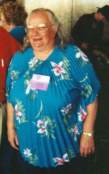 A cheerful woman in a vibrant floral shirt smiles in a social setting surrounded by attendees.