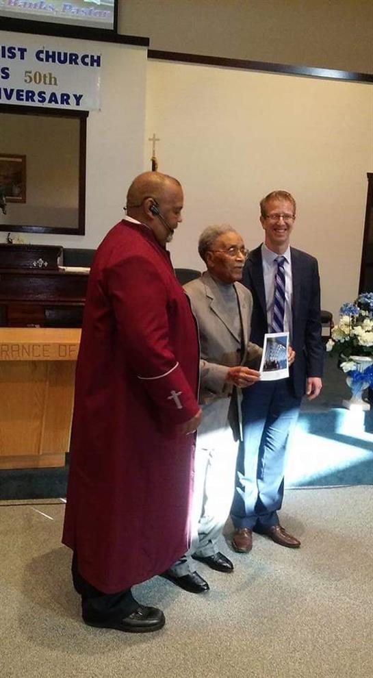 Community leaders gather with an elder, holding a photo, celebrating a special occasion in a church.