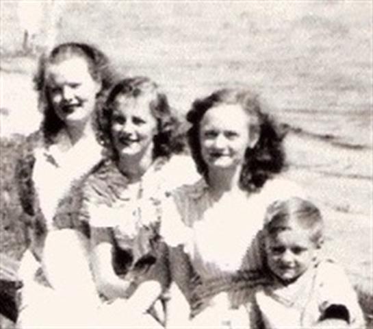 Five people relax together at the shoreline, smiling and enjoying a warm summer day by the water.