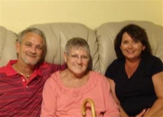Three family members sit on a couch, smiling together in a cozy living room.