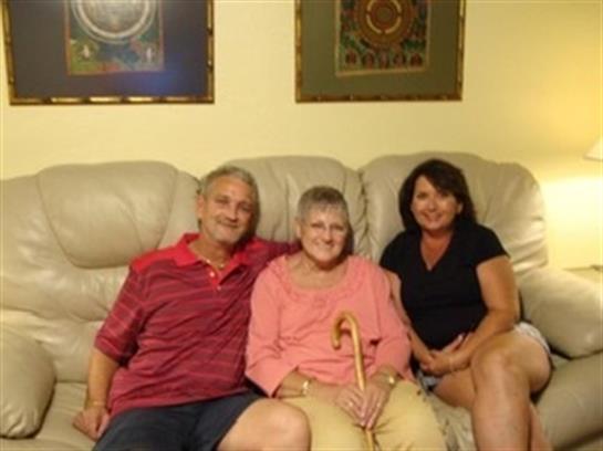Three family members sit closely on a couch, sharing happy moments in a warm living room.