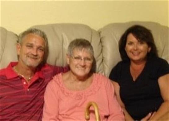 Three family members sit together on a couch, sharing laughter and affection during a cozy visit.