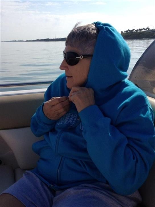 A senior woman adjusts her blue hoodie while relaxing on a boat in the bright sunlight.
