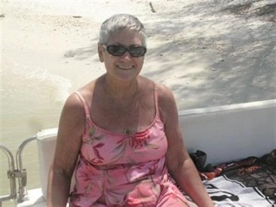 A joyful woman in a pink dress and sunglasses relaxes on a boat by a beautiful beach.