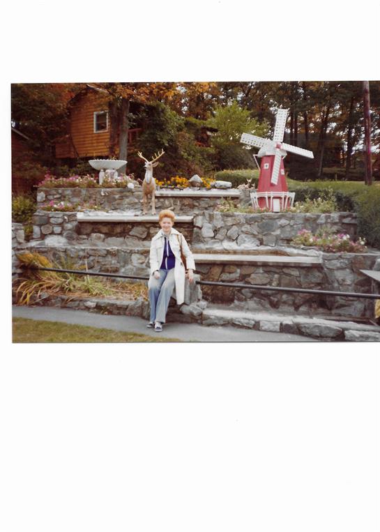A woman relaxes on landscaped stone steps amidst colorful autumn foliage and decorations.