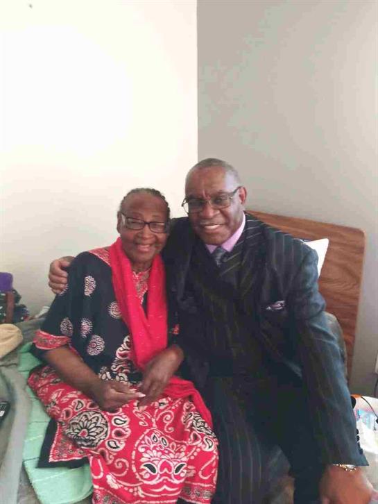 Two smiling individuals share a warm moment while sitting comfortably in a bright, intimate room.