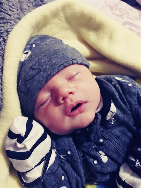 A baby boy with a blue hat sleeps quietly in a soft blanket, enjoying a peaceful moment indoors.