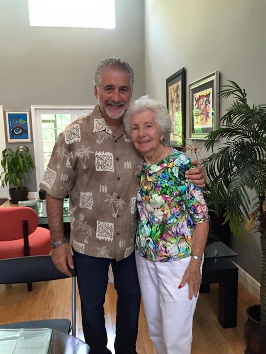 Two friends happily embrace in a bright living room filled with art and plants.