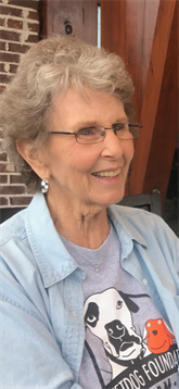 A happy elderly woman enjoys a lively conversation at an outdoor cafe with friends.