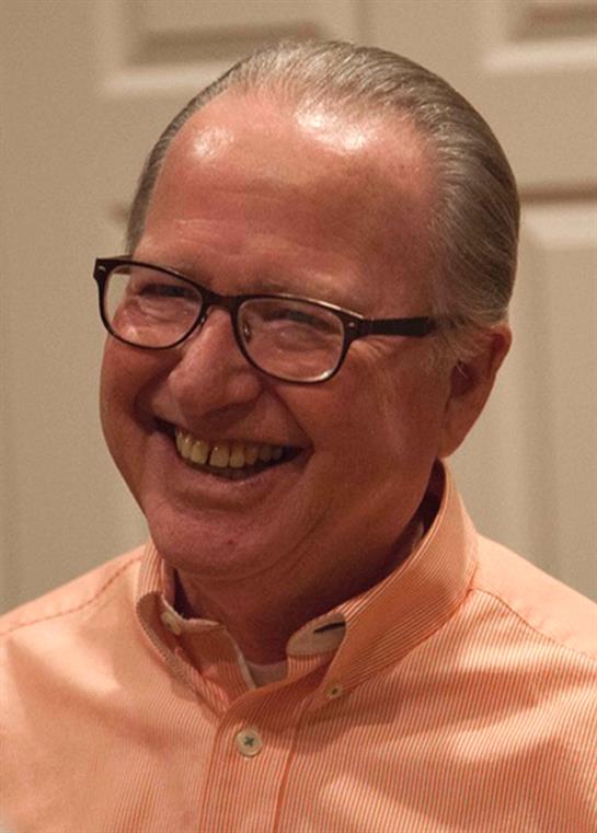 Man with glasses smiles broadly, enjoying a lighthearted moment at a social gathering.