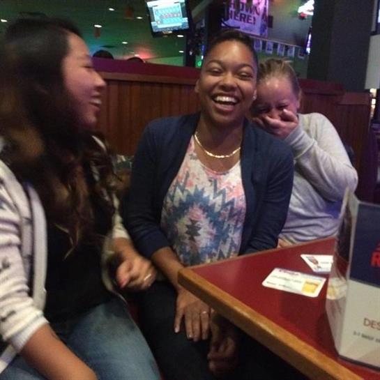 Three friends share laughter and smiles at a busy restaurant during an evening gathering.
