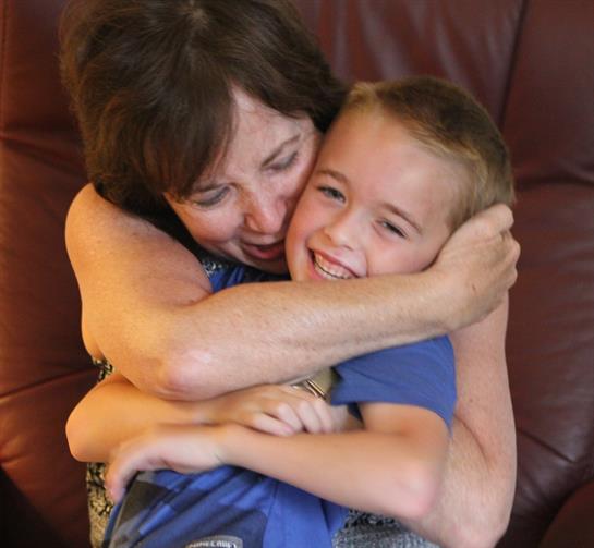 A woman joyfully hugs a smiling boy while sitting on a couch, sharing a special moment together.