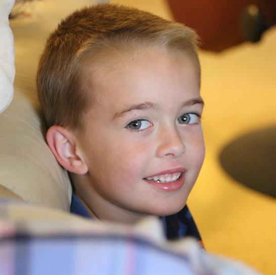 A smiling blonde boy relaxes at home, enjoying his time indoors.