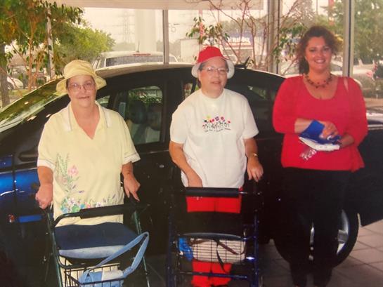 Three women stand with shopping carts, enjoying their time outside a car under bright sunlight.