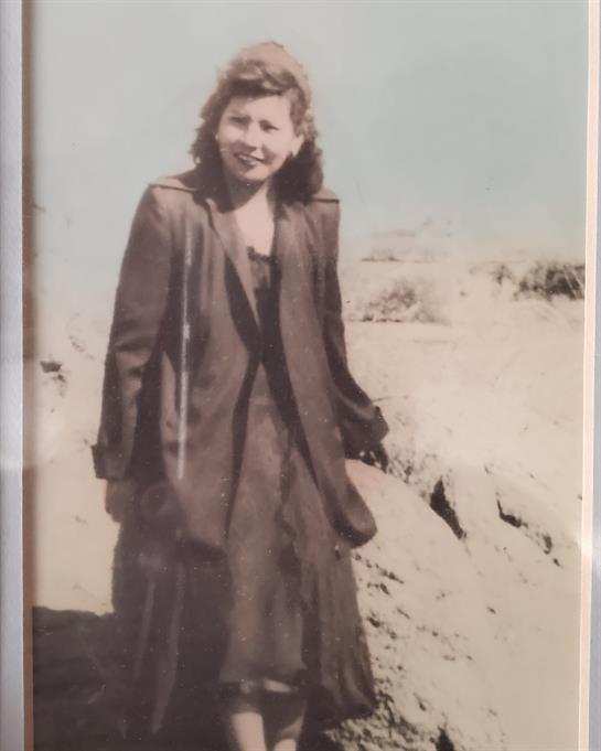 A young woman smiles gracefully on the shore with waves rolling behind her.