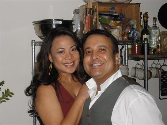 A joyful couple poses closely together, sharing smiles at a relaxed gathering in their home.