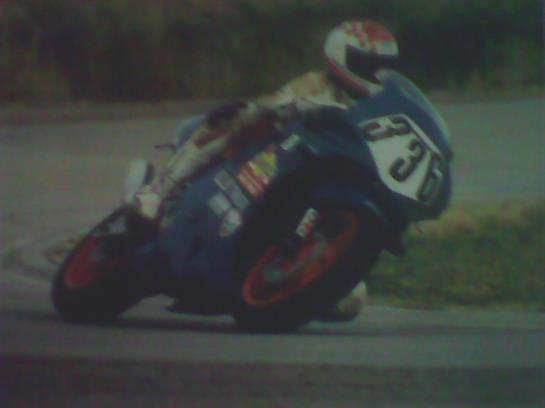 A motorcyclist makes a precise turn on a racetrack with fans watching under clear skies.