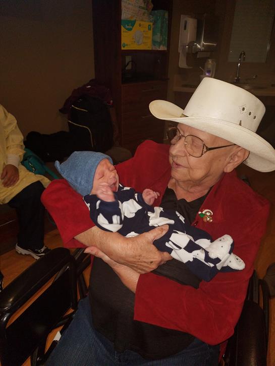 An older man in a white hat cuddles a newborn in a warm family gathering filled with love.