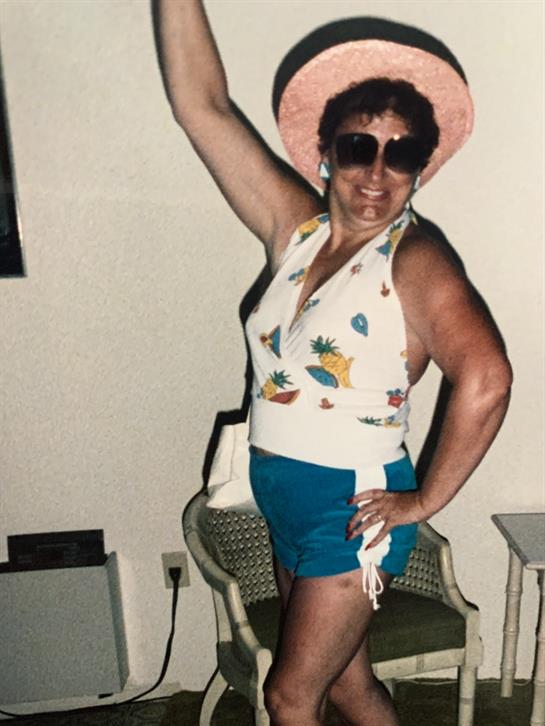 A woman joyfully poses in a bright swimsuit and hat, showcasing her summer spirit.