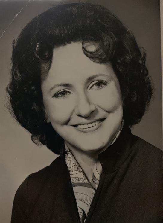 A woman with curly hair smiles warmly, showcasing a classic portrait style with a soft backdrop.