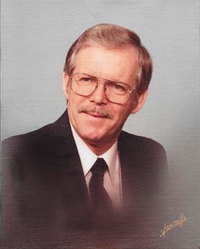 A gentleman in a suit and tie poses for a professional portrait, smiling pleasantly.