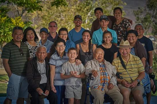 A diverse group of family members gathers happily outdoors in a park setting.