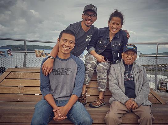 Four family members smile together on a dock, enjoying each other's company on a cloudy day.