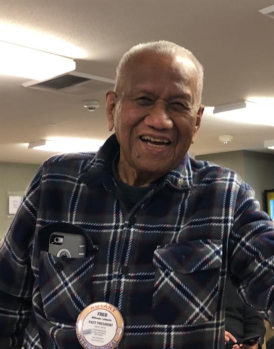 An elderly man, dressed in a plaid shirt, joyfully engages with others and holds a treat.