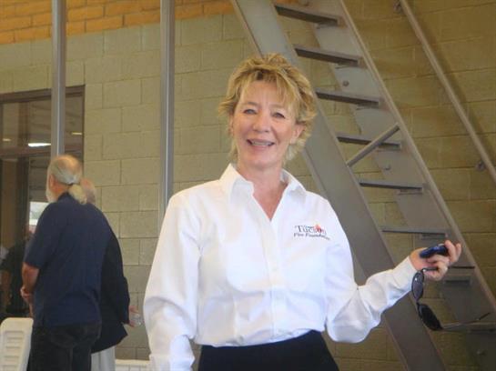 A woman in a white shirt and black skirt warmly greets guests at a conference.